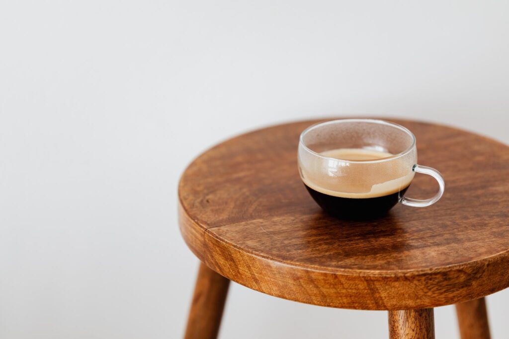 Wide cup of fresh black coffee placed on small brown wooden table near white wall