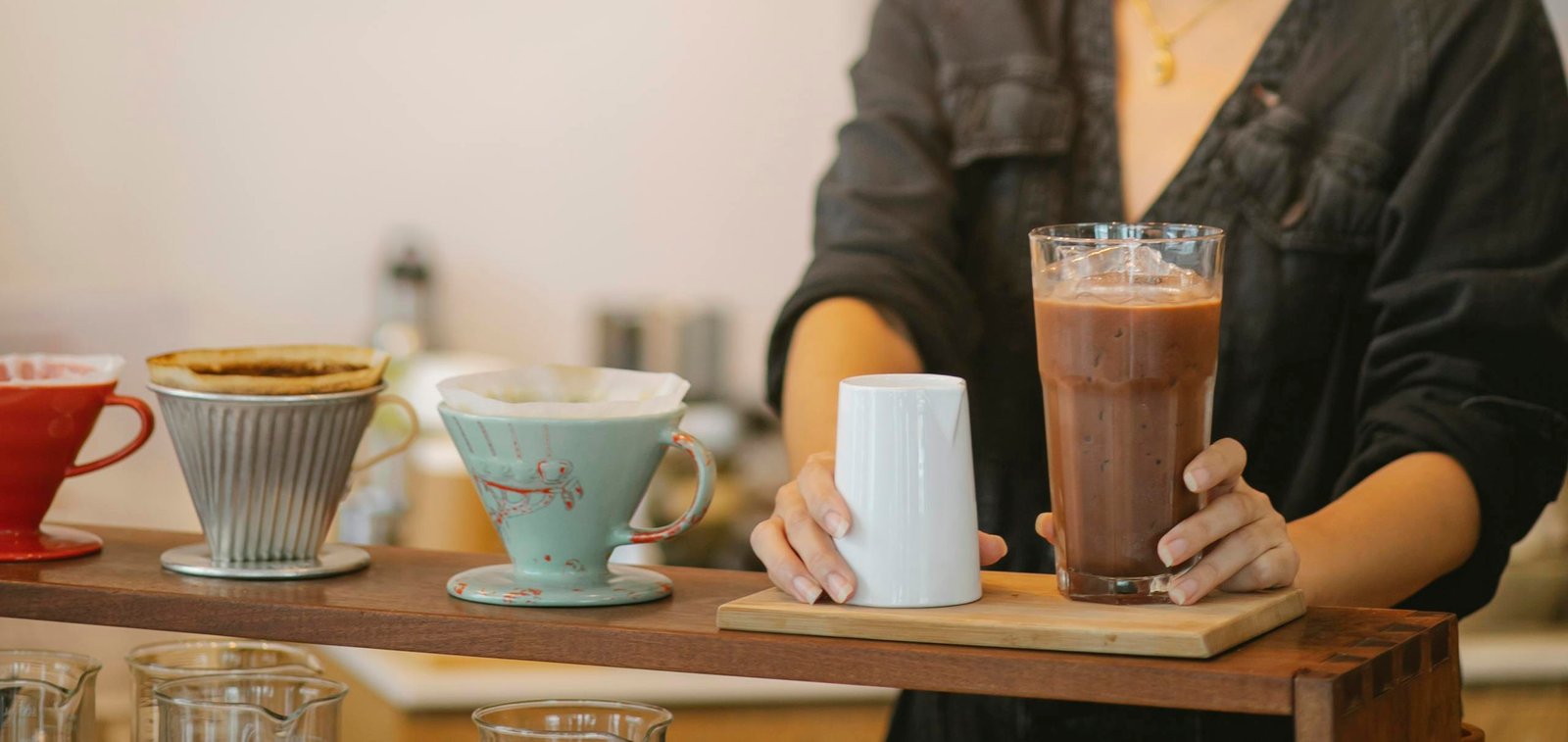 A barista prepares an iced coffee using drip filters in a coffee shop setting.